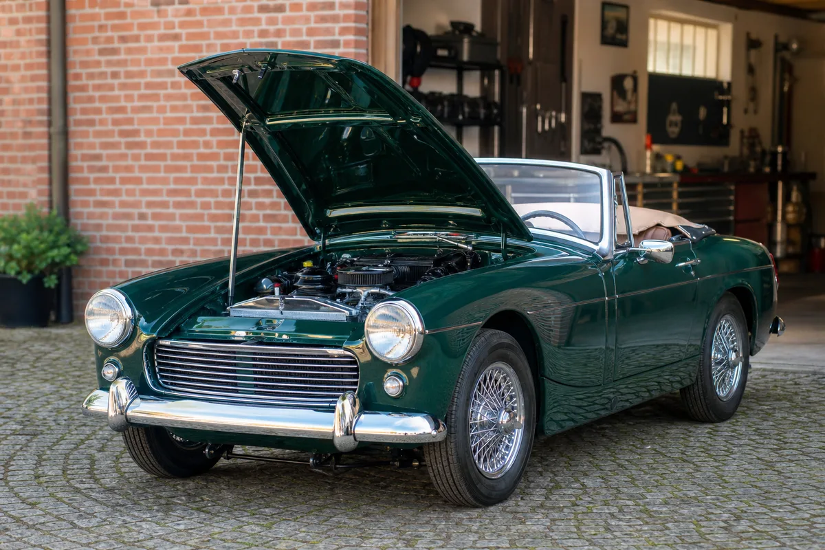 Voiture ancienne restaurée à la carrosserie repeinte garée devant un garage, capot ouvert laissant voir le compartiment moteur propre
